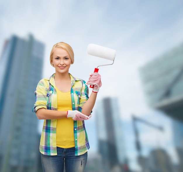 concepto de reparación, construcción y mantenimiento - mujer sonriente en guantes con rodillo de pintura