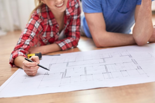 Foto concepto de reparación, construcción, renovación y personas - cerca de una pareja feliz mirando el plano en casa