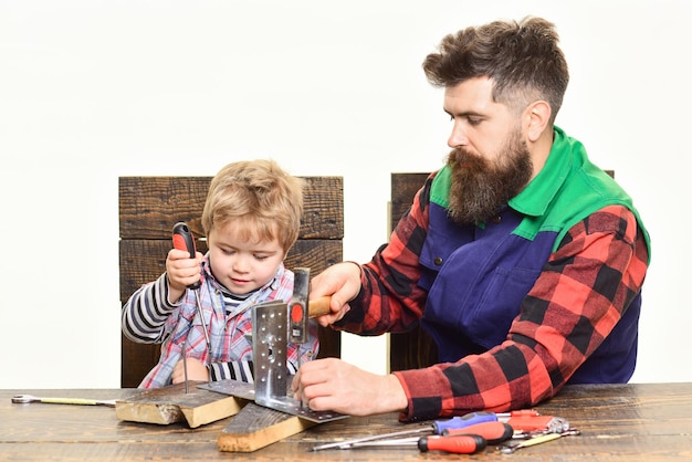 Concepto de reparación. Niño con destornillador. Asistente. Trabajador barbudo. Reparador en uniforme. Platos de metal. Reparar. Hombre barbudo con poca ayuda. Creatividad infantil Padre e hijo en taller.