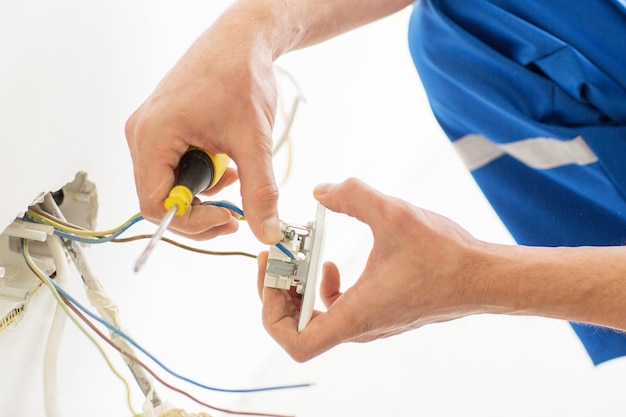 Foto concepto de reparación, renovación, electricidad y personas - cierre de manos de electricista con enchufe de fijación de destornillador