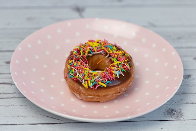 Concepto de repostería. Donuts con glaseado de chocolate con chispas de colores, sobre una placa rosa. Vista superior