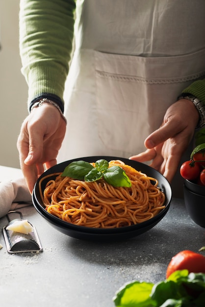 Concepto de restaurante. Hombre cocinando espaguetis italianos con tomate y albahaca, imagen de enfoque selectivo