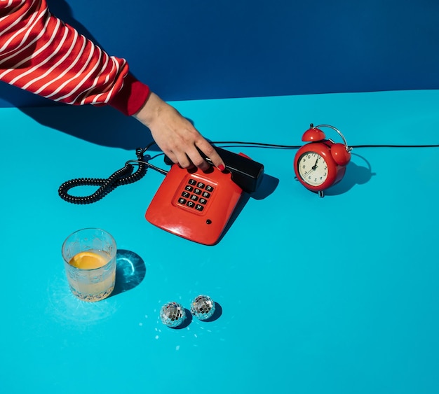 Concepto retro mínimo con mano, teléfono vintage rojo, vaso, reloj y bolas de discoteca