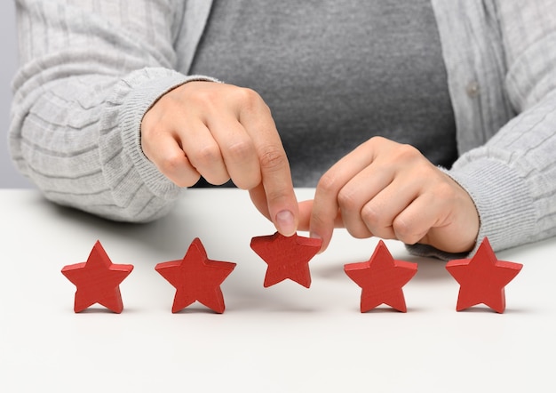 Foto concepto de retroalimentación de la experiencia del cliente. cinco estrellas rojas, la mejor calificación de excelentes servicios con una mano femenina para cumplir. mesa blanca