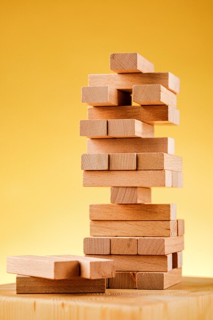 El concepto de riesgo empresarial con el modelo jenga. Bloques de madera sobre un fondo amarillo.