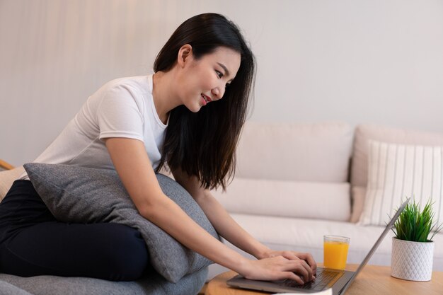 Concepto de sala de estar en la cafetería una chica con un moño usando su computadora portátil en Internet con un vaso de jugo de naranja.