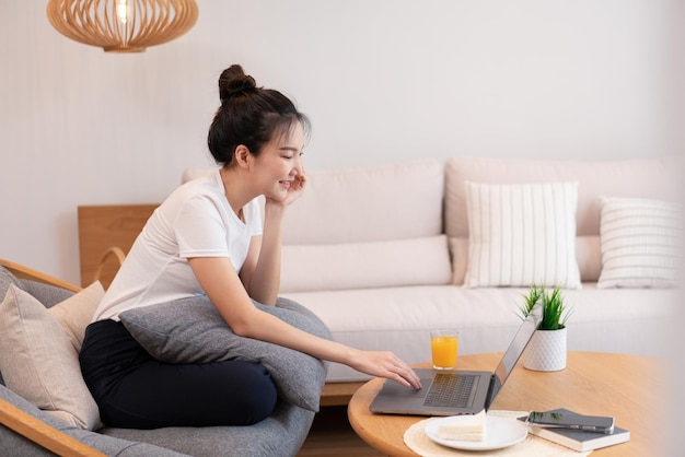 Concepto de sala de estar en la cafetería una chica con un moño usando su computadora portátil en Internet con un vaso de jugo de naranja.