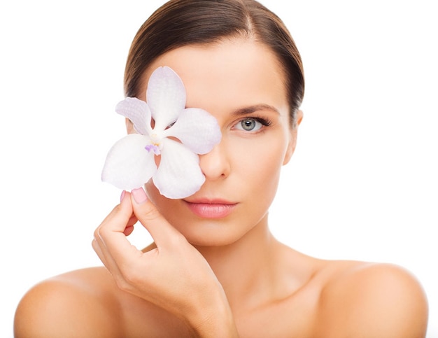 Concepto de salud y belleza - mujer relajada con flor de orquídea sobre el ojo