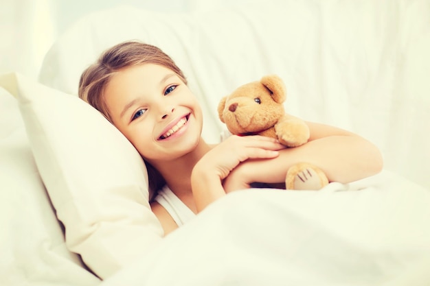 Concepto de salud y belleza - niña con osito de peluche durmiendo en casa