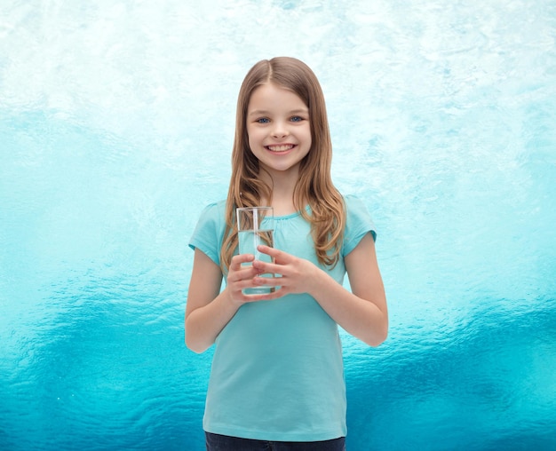 concepto de salud y belleza - niña sonriente con un vaso de agua