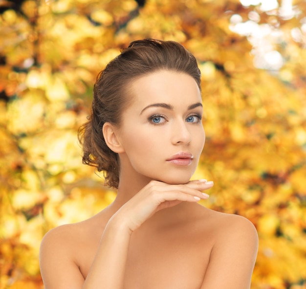Concepto de salud y belleza: rostro y manos de mujer hermosa con updo sobre fondo amarillo de hojas de otoño