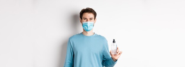 Concepto de salud y cuarentena de covid retrato de hombre sonriente con máscara médica que muestra desinfectante de manos b