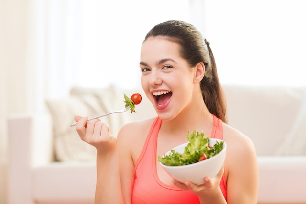 concepto de salud, dieta, hogar y felicidad - adolescente deportiva sonriente con ensalada verde en casa