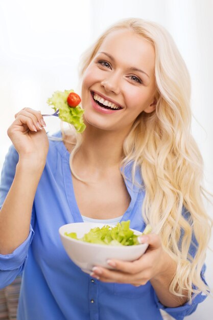 concepto de salud, dieta, hogar y felicidad - mujer joven sonriente con ensalada verde en casa