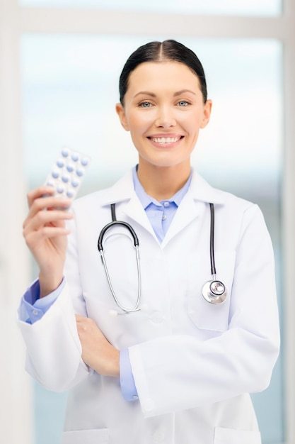 concepto de salud, farmacia y medicina - joven médico sonriente con pastillas y estetoscopio en el gabinete