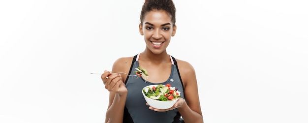 Concepto de salud y fitness Hermosa dama africana americana en ropa de fitness en dieta comiendo ensalada fresca Aislada sobre fondo blanco
