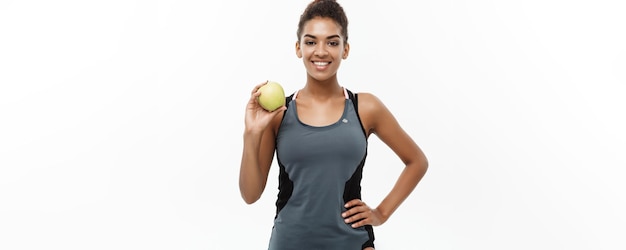 Foto concepto de salud y fitness hermosa dama africana americana en ropa de fitness gris con manzana verde aislada sobre fondo blanco