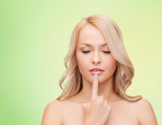 concepto de salud, gente y belleza - hermosa mujer joven tocando sus labios sobre fondo verde