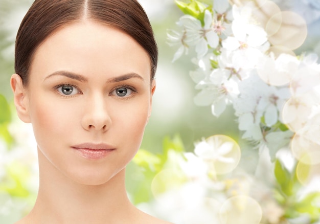 concepto de salud, gente, eco y belleza - hermosa cara de mujer joven sobre fondo de jardín floreciente verde