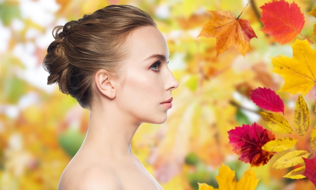 concepto de salud, gente, temporada y belleza - hermosa cara de mujer joven sobre fondo de hojas de otoño