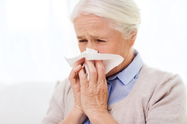 concepto de salud, gripe, higiene, edad y personas - anciana enferma que sopla la nariz a la servilleta de papel en casa