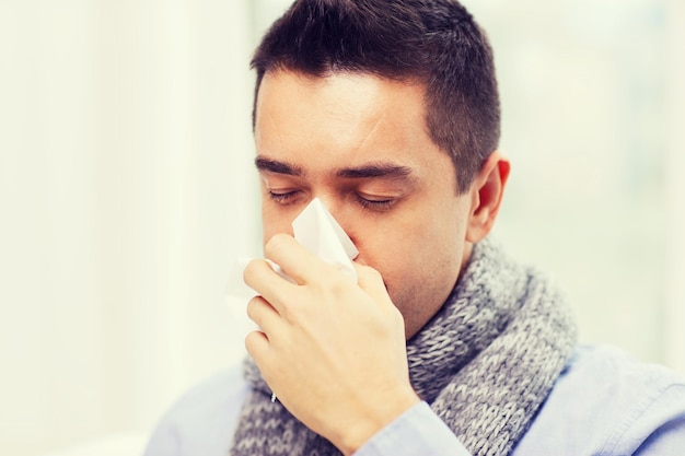 Foto concepto de salud, gripe, personas, rinitis y medicina - cierre de un hombre enfermo que se sopla la nariz con una servilleta de papel en casa