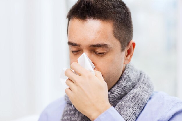 concepto de salud, gripe, personas, rinitis y medicina - cierre de un hombre enfermo que se sopla la nariz con una servilleta de papel en casa