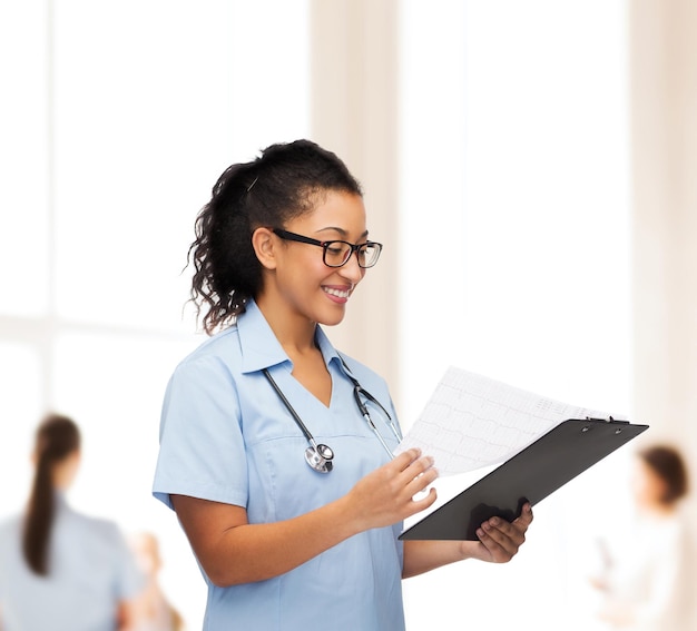 concepto de salud y medicina - doctora o enfermera afroamericana sonriente en anteojos con estetoscopio y portapapeles