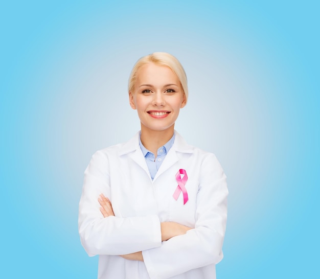 concepto de salud y medicina - doctora sonriente con cinta rosa de concientización sobre el cáncer sobre fondo azul