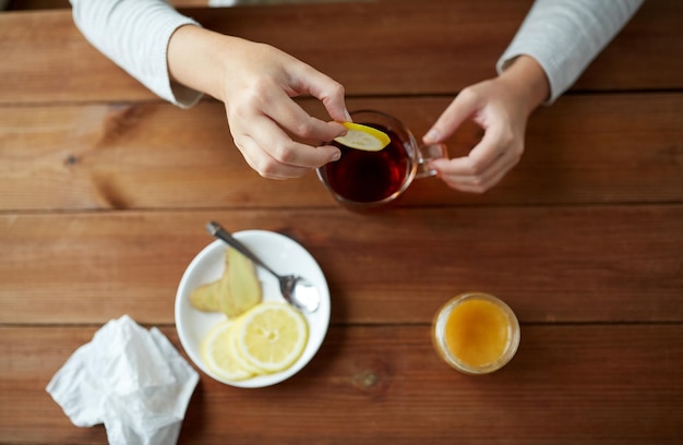 concepto de salud, medicina tradicional y etnociencia - cierre de una mujer añadiendo limón a la taza de té