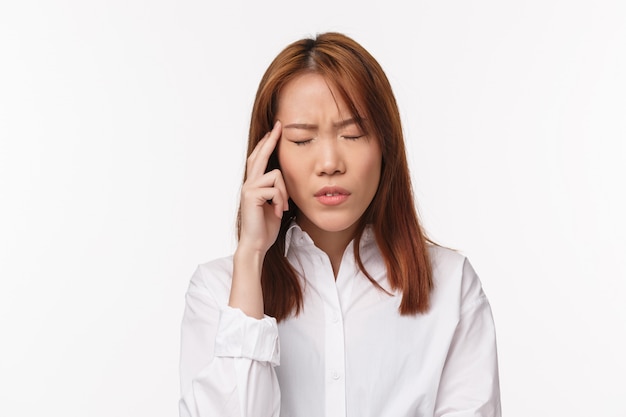 Concepto de salud, midicina y personas. Close-up retrato de mujer asiática joven cansada y mareada que sufre dolor de cabeza, cerrar los ojos y tocar la sien, mueca sensación dolorosa, tiene migraña,