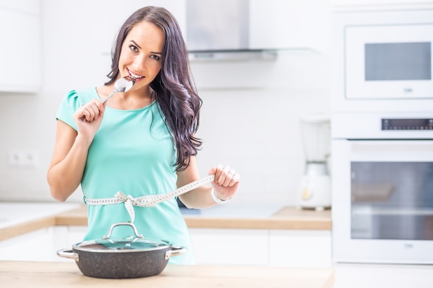 Concepto de salud y pérdida de peso de dieta - hermosa mujer joven con cinta métrica en su cocina.