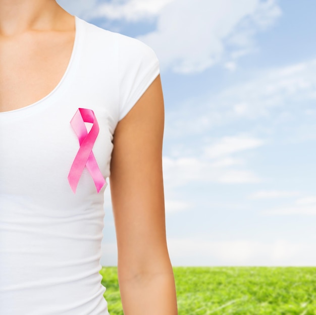 concepto de salud, personas, caridad y medicina - cierre de una mujer en camiseta con una cinta rosa de concientización sobre el cáncer de mama sobre el cielo azul y el fondo de la hierba