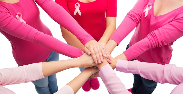 concepto de salud, personas, gestos y medicina - cierre de mujeres con camisas en blanco con cintas rosas de concientización sobre el cáncer de mama poniendo las manos encima sobre fondo blanco