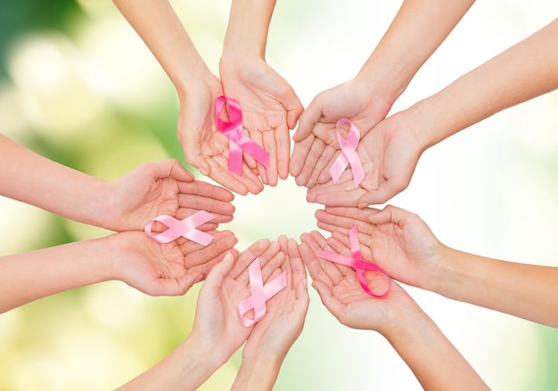 Foto concepto de salud, personas y medicina - cierre de las manos de las mujeres con cintas de concienciación sobre el cáncer sobre fondo verde