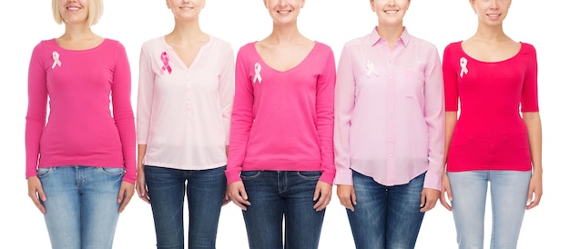 El concepto de salud, personas y medicina: el cierre de mujeres sonrientes con camisas en blanco y cintas rosas de concienciación sobre el cáncer de mama sobre fondo blanco.