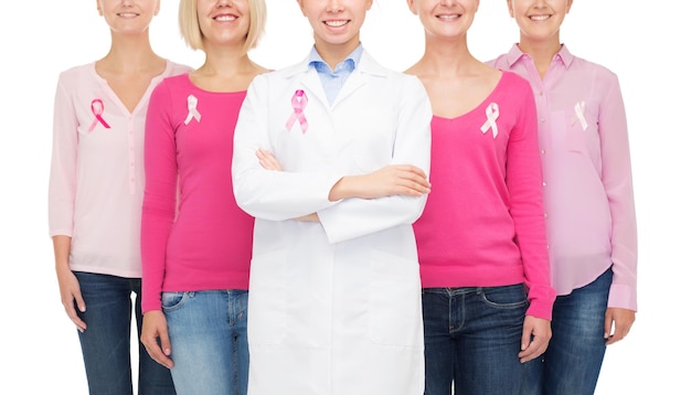 El concepto de salud, personas y medicina: el cierre de mujeres sonrientes con camisas en blanco y cintas rosas de concienciación sobre el cáncer de mama sobre fondo blanco.