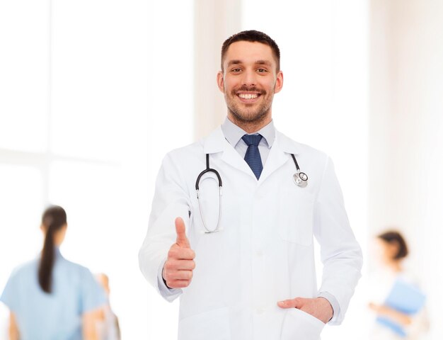 El concepto de salud, profesión y medicina: un médico sonriente con estetoscopio que muestra los pulgares hacia arriba sobre el fondo blanco