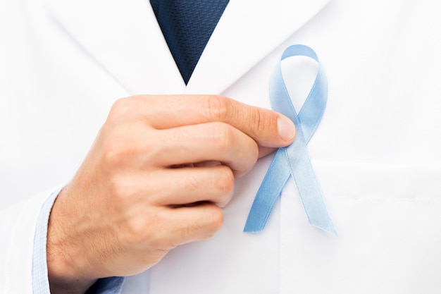 Foto concepto de salud, profesión, personas y medicina - cierre de la mano de un médico varón con una cinta azul cielo de concienciación sobre el cáncer de próstata