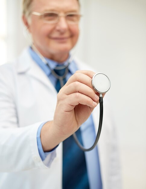 concepto de salud, profesión, personas y medicina - cierre de un médico feliz con bata blanca con estetoscopio en el consultorio médico