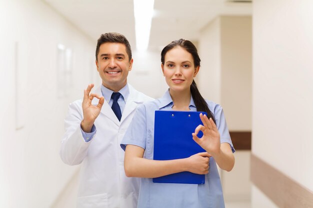 concepto de salud, profesión, personas y medicina - médico y enfermera sonrientes con portapapeles mostrando el signo de la mano en el hospital