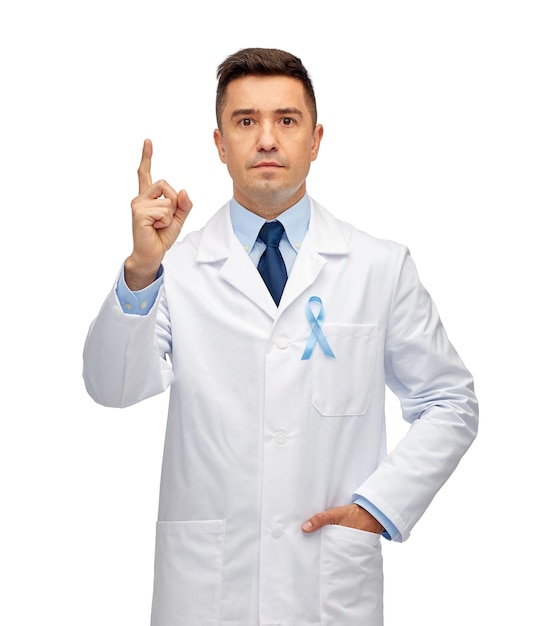 concepto de salud, profesión, personas y medicina - médico masculino con bata blanca con cinta azul cielo de concienciación sobre el cáncer de próstata apuntando con el dedo hacia arriba