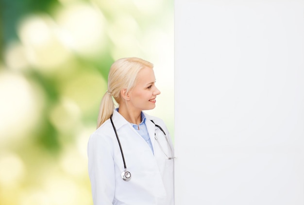 concepto de salud, publicidad, personas y medicina - doctora sonriente con estetoscopio mirando algo sobre el fondo natural