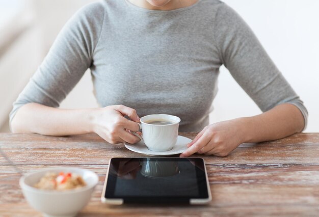 concepto de salud, tecnología, internet, comida y hogar - cerca de una mujer tomando café y usando una computadora de tablet pc