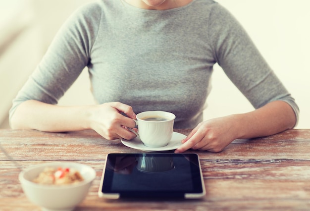 concepto de salud, tecnología, internet, comida y hogar - cerca de una mujer tomando café y usando una computadora de tablet pc