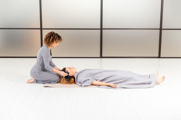 Concepto saludable de bienestar. Meditación de dos mujeres en el suelo. Relájese y zen en la sala blanca. Cuidado del cuerpo.