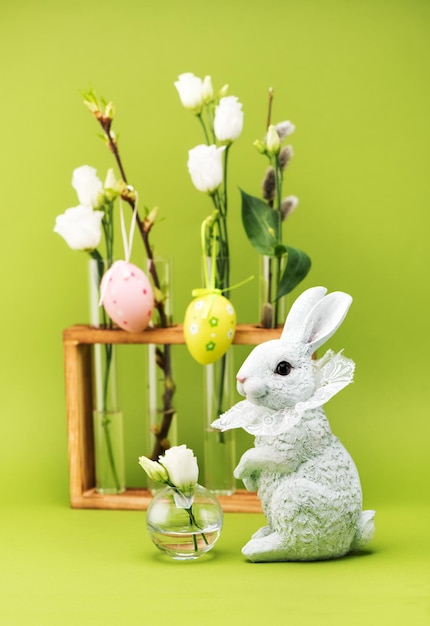 Concepto de saludo de Pascua. Conejito de Pascua y flores blancas de primavera en jarrones sobre un fondo verde.