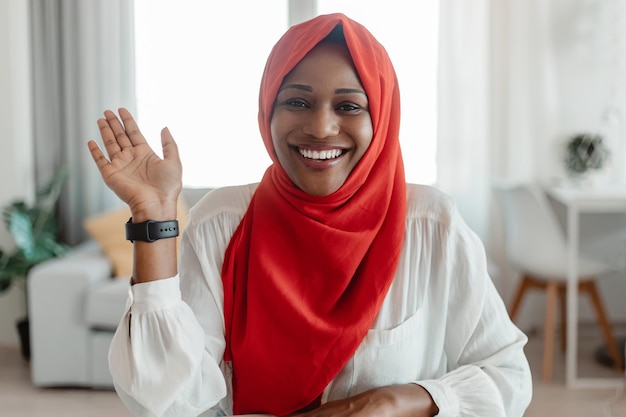 Concepto de saludo Retrato de mujer musulmana negra feliz saludando y sonriendo a la cámara usando una computadora portátil en la oficina en casa