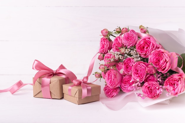 Concepto de San Valentín. Rosas rosas y cajas de regalo con cintas sobre mesa de madera blanca.