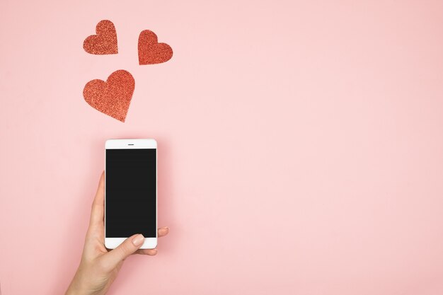 Foto concepto de san valentín, teléfono móvil en la pantalla de la mano con corazones rojos en la superficie de color rosa. amor en las redes sociales